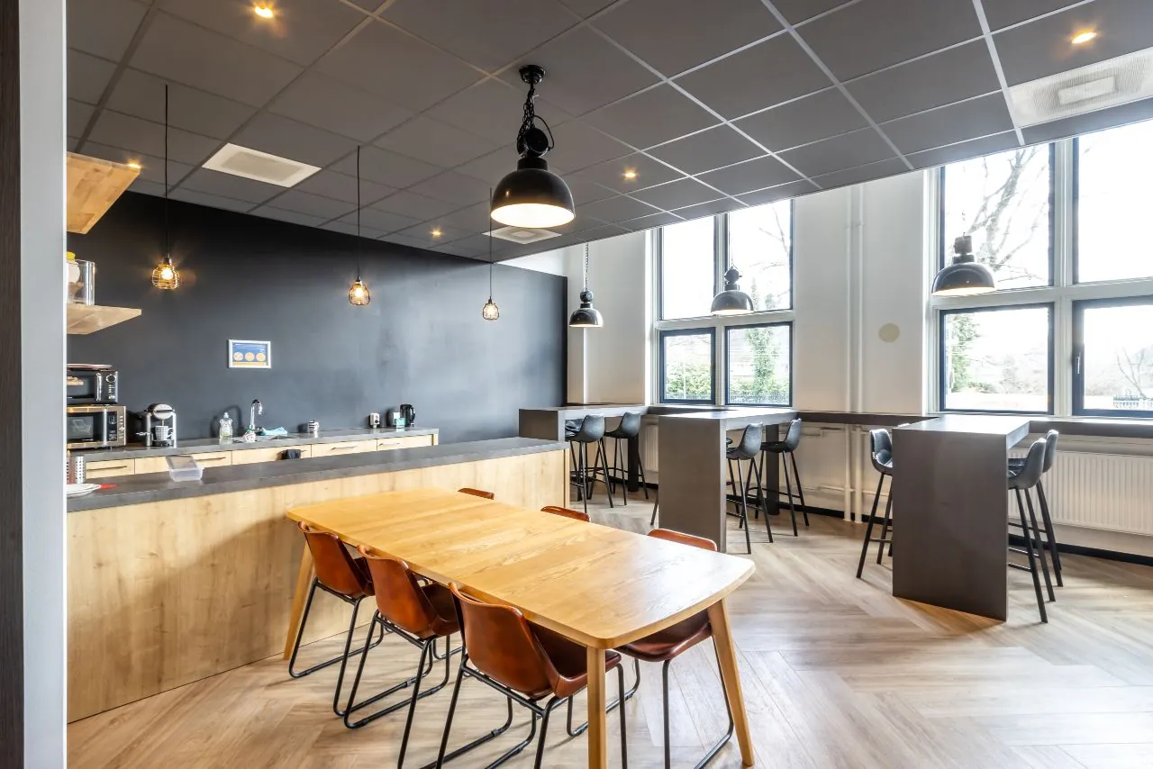 Moderne kantine met houten meubels, zwarte accenten en grote ramen aan de Lage Naarderweg.